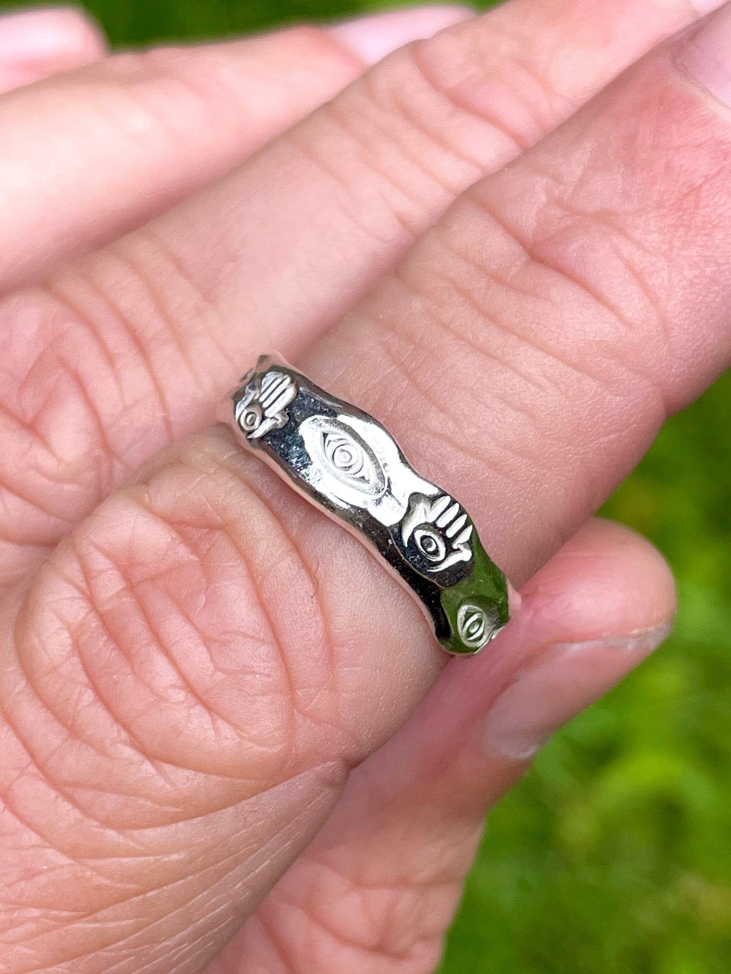 Angled view of recycled silver ring with hand-stamped hamsa and eye designs