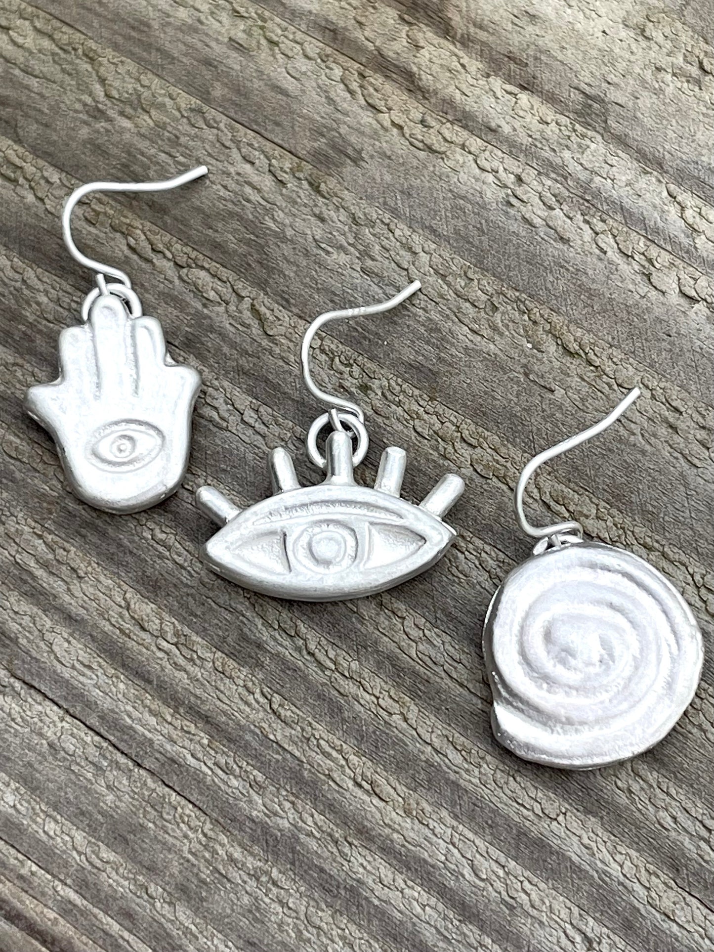 Hamsa hand, eye, spiral earrings on wooden bench