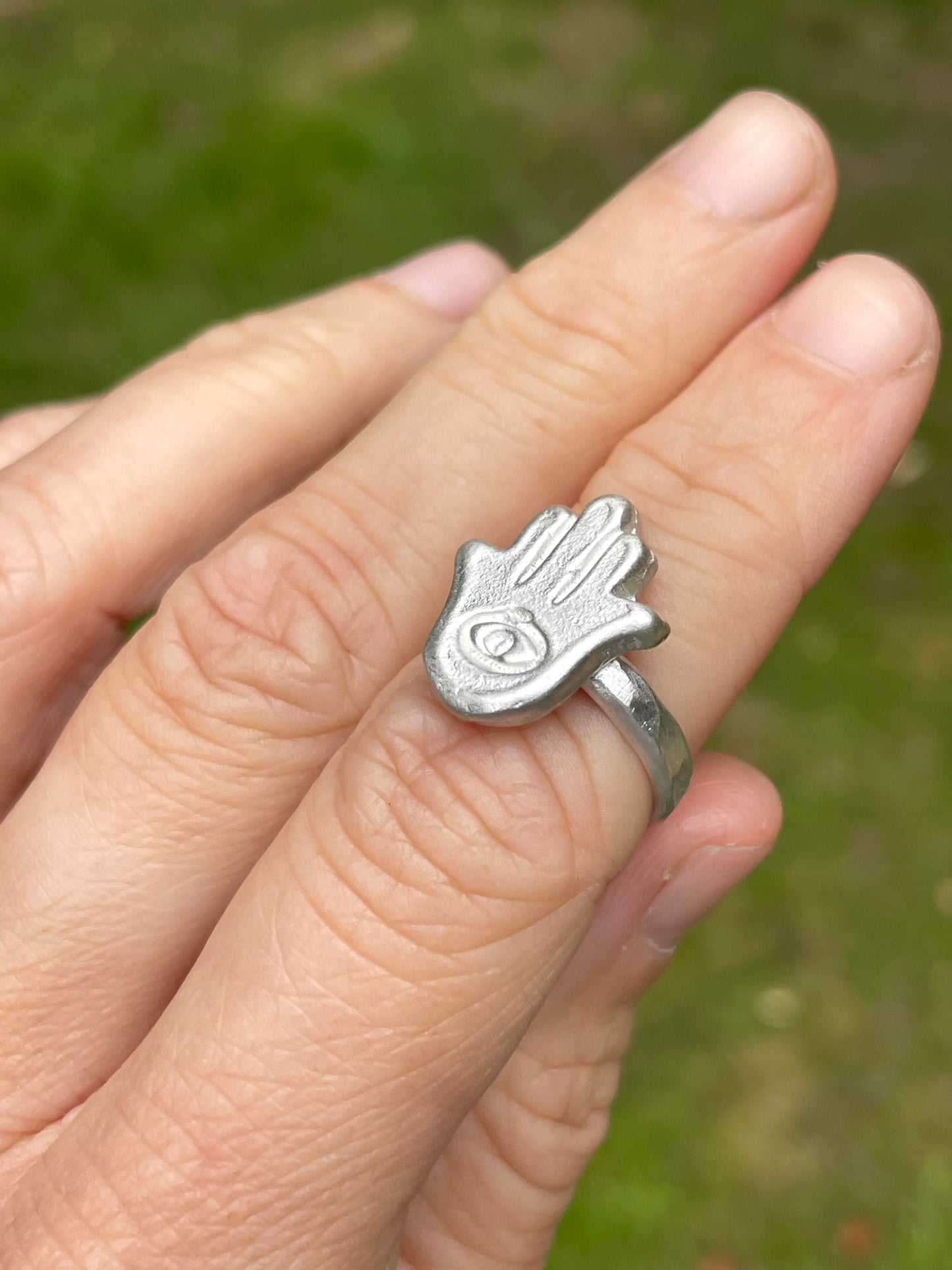 Silver sandcast Hamsa hand ring on a person's finger with a blurred green background