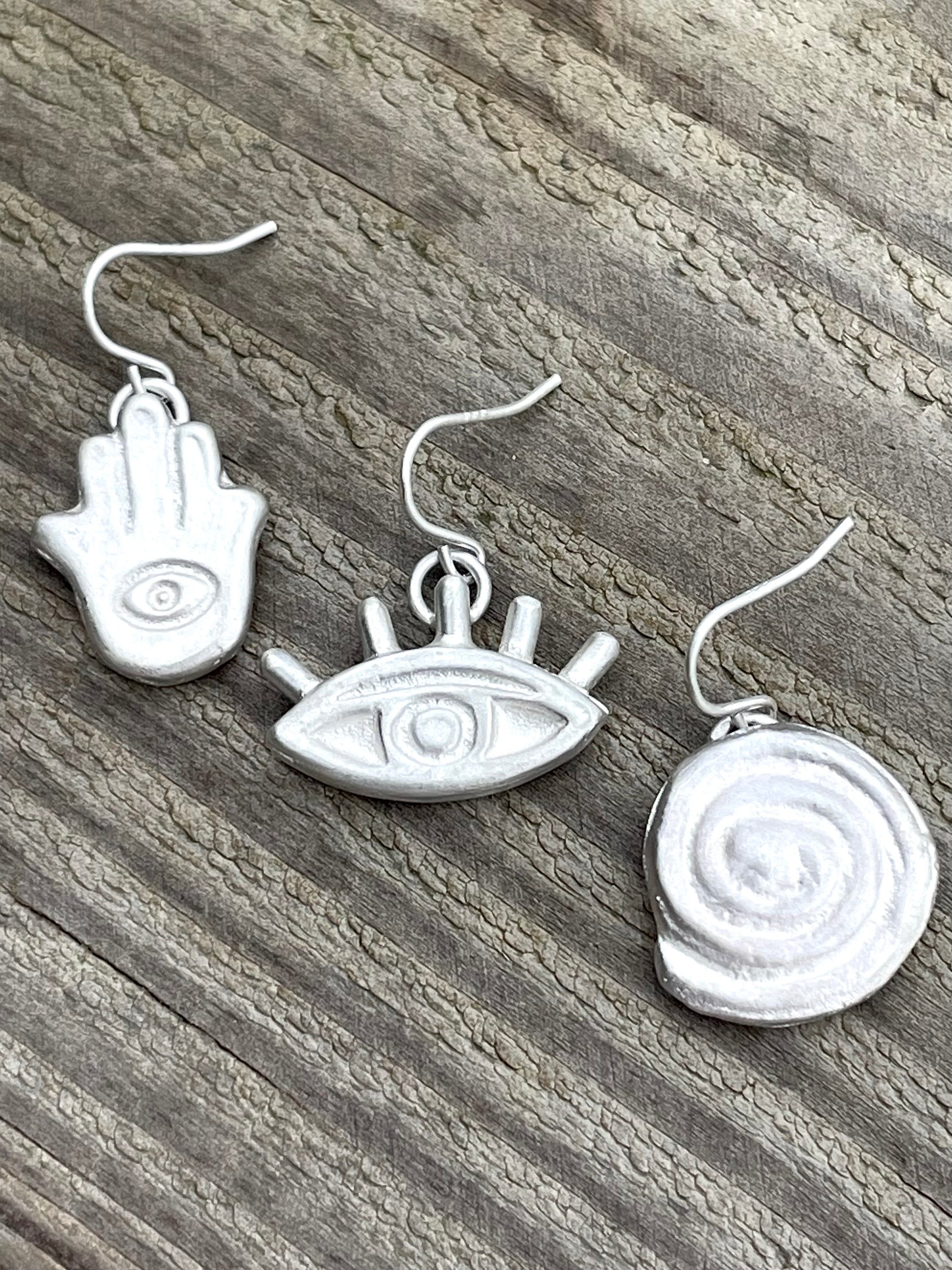 Hamsa hand, eye, spiral earrings on wooden bench