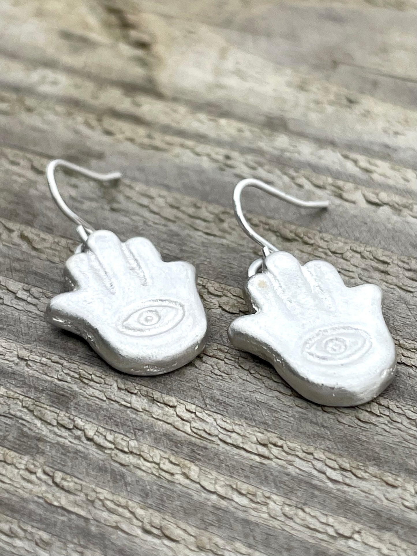 Silver sandcast hamsa hand-shaped earrings on a wooden surface