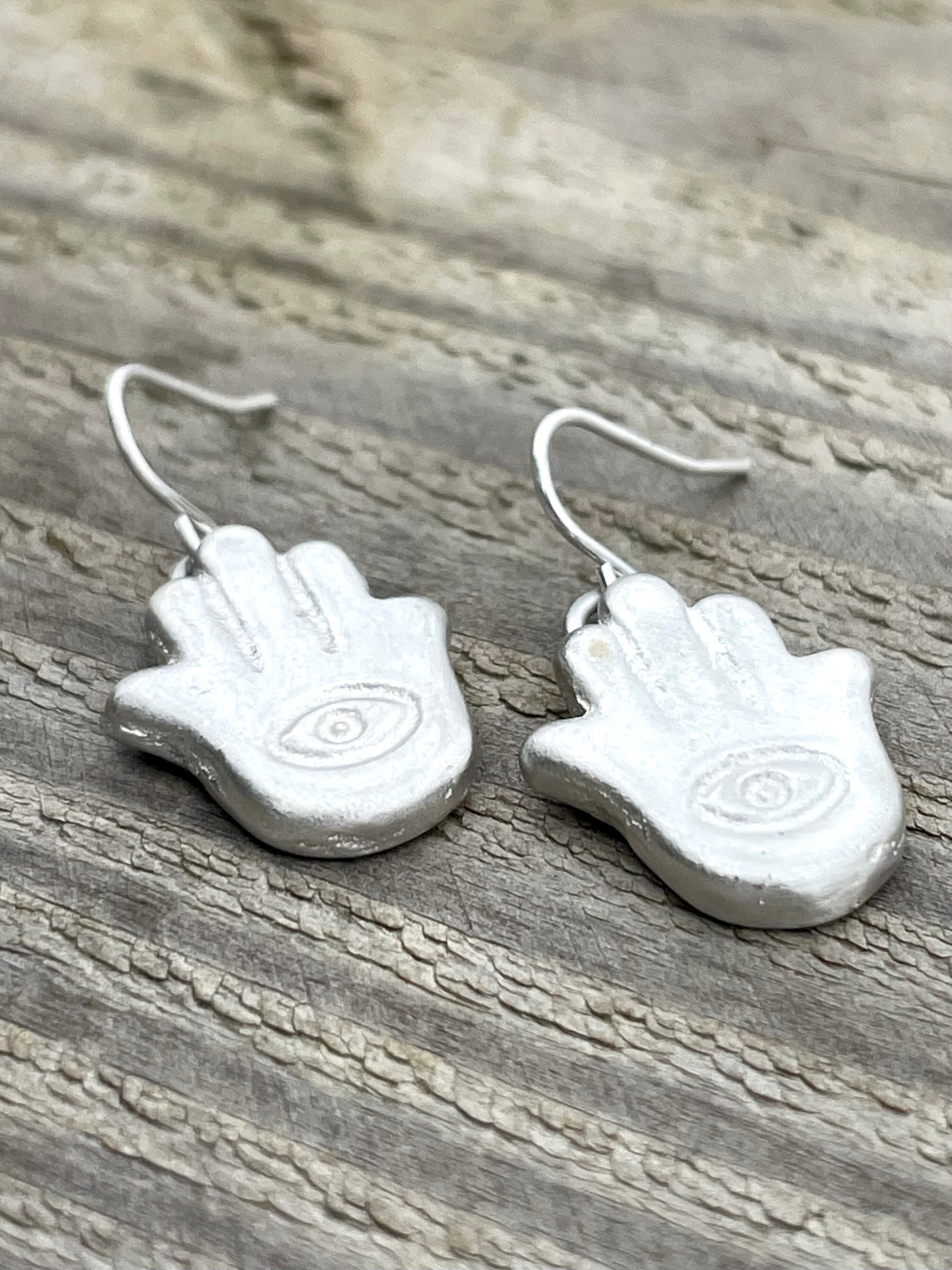 Silver sandcast hamsa hand-shaped earrings on a wooden surface