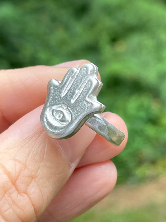 Silver sandcast Hamsa hand ring held in a hand with a blurred green background