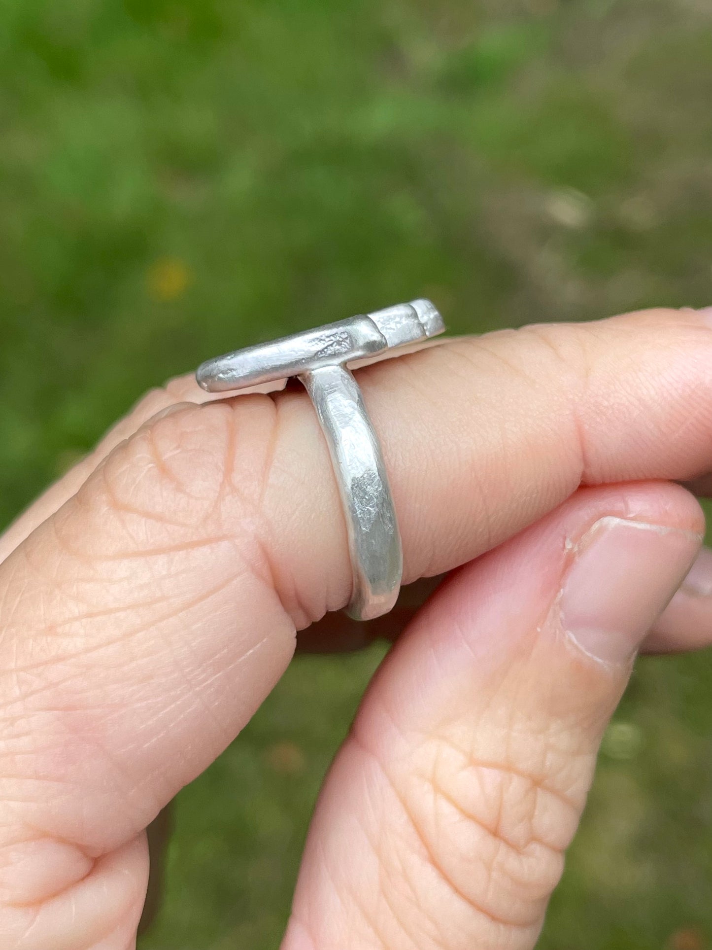 Silver ring on a finger with a blurred green background