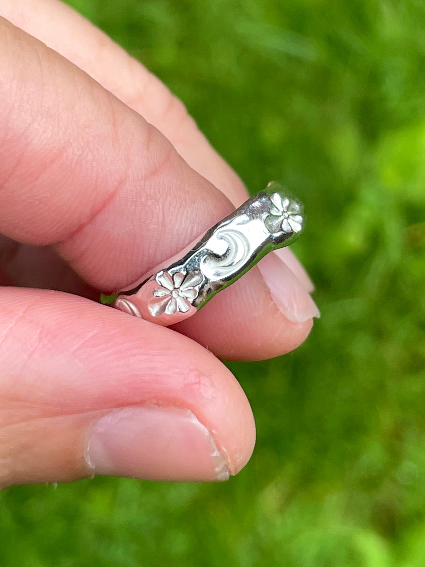 Angled view of recycled silver band with hand-stamped moon and star motifs showing textured detail