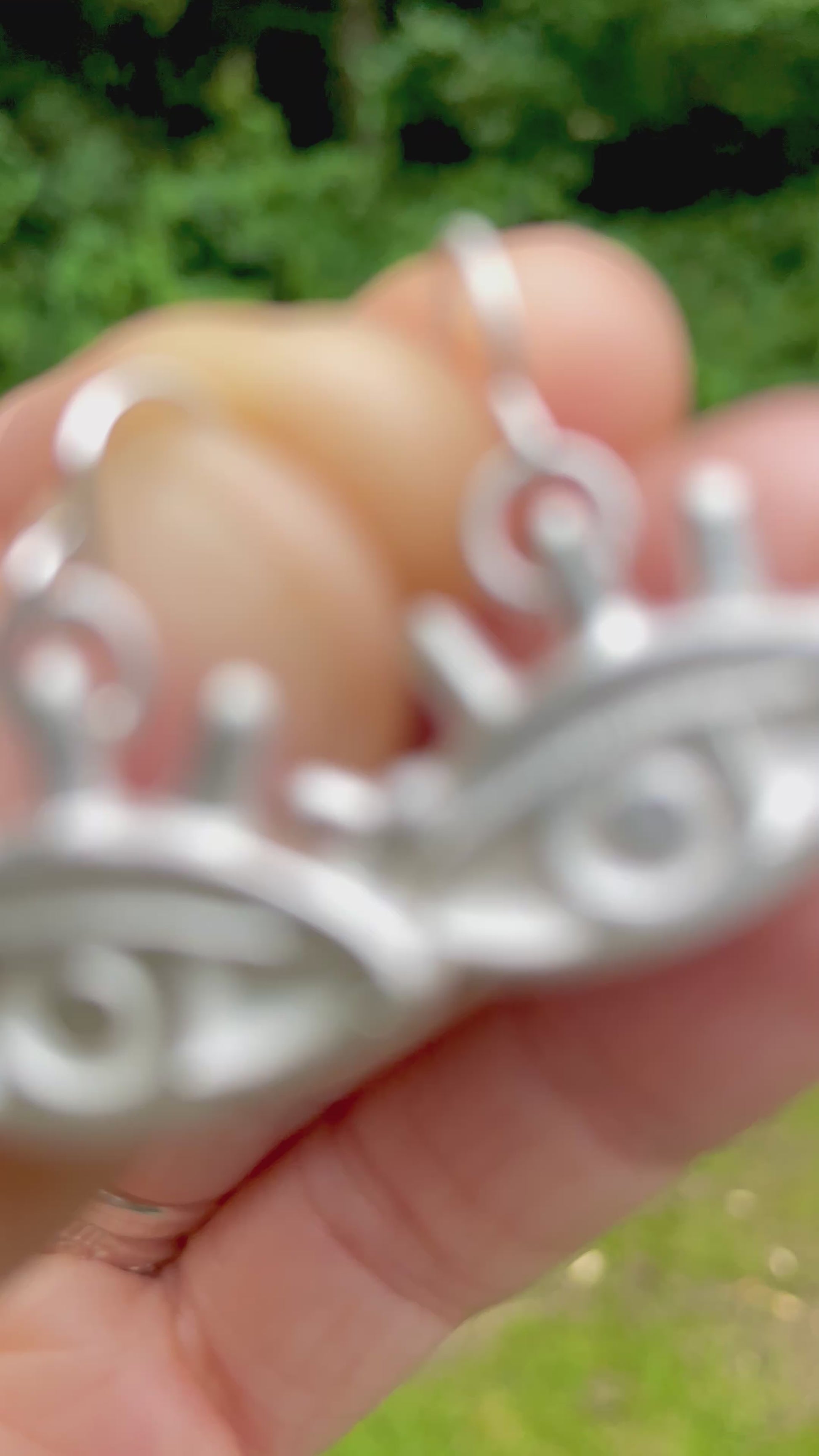 silver sandcast eye shaped earrings held in a hand with a blurred green grass background