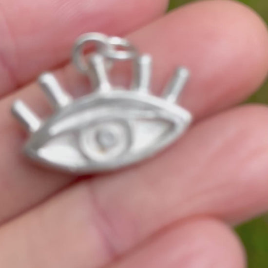 silver sandcast eye pendant on a hand with green grassy backgound