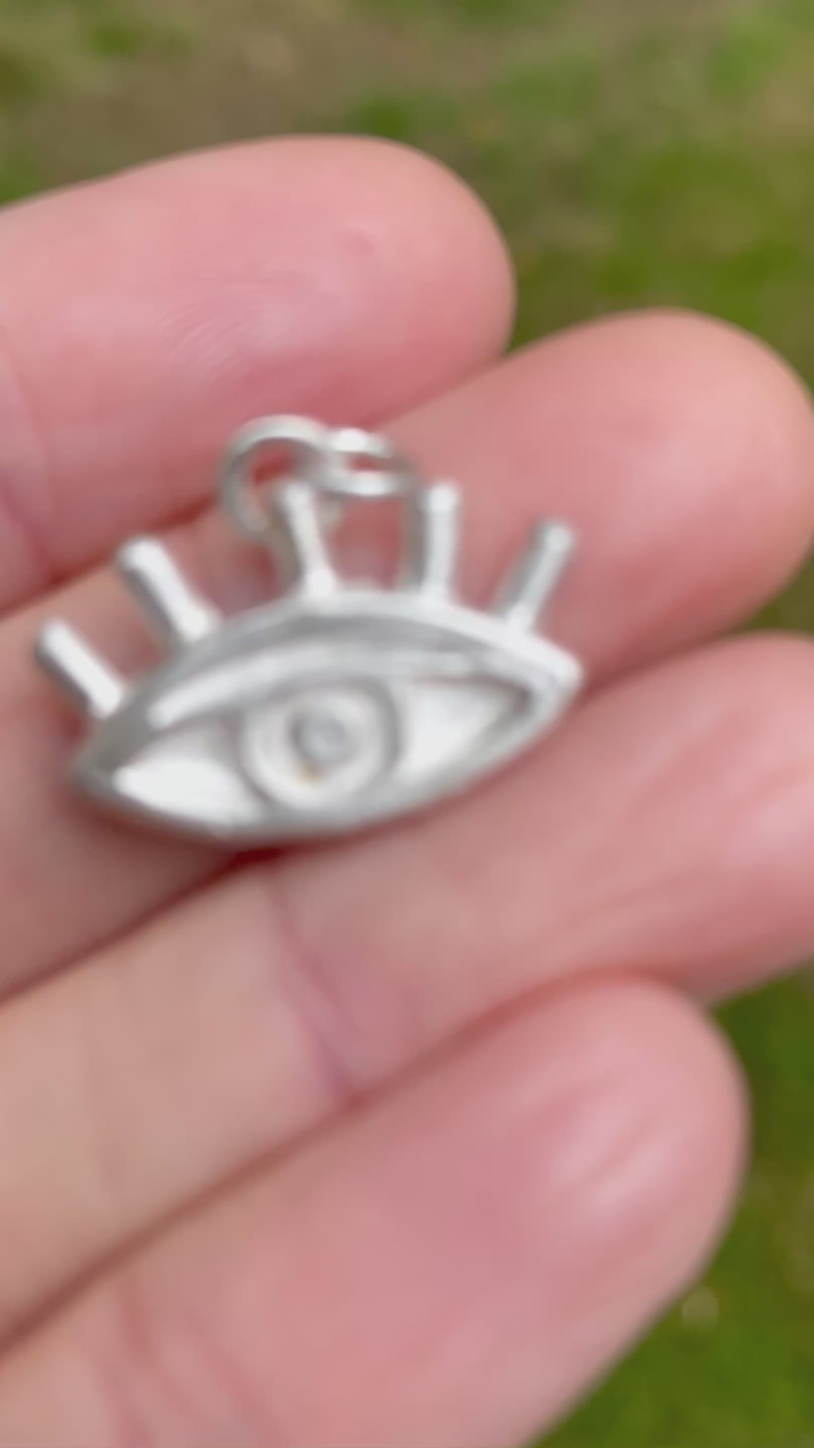 silver sandcast eye pendant on a hand with green grassy backgound