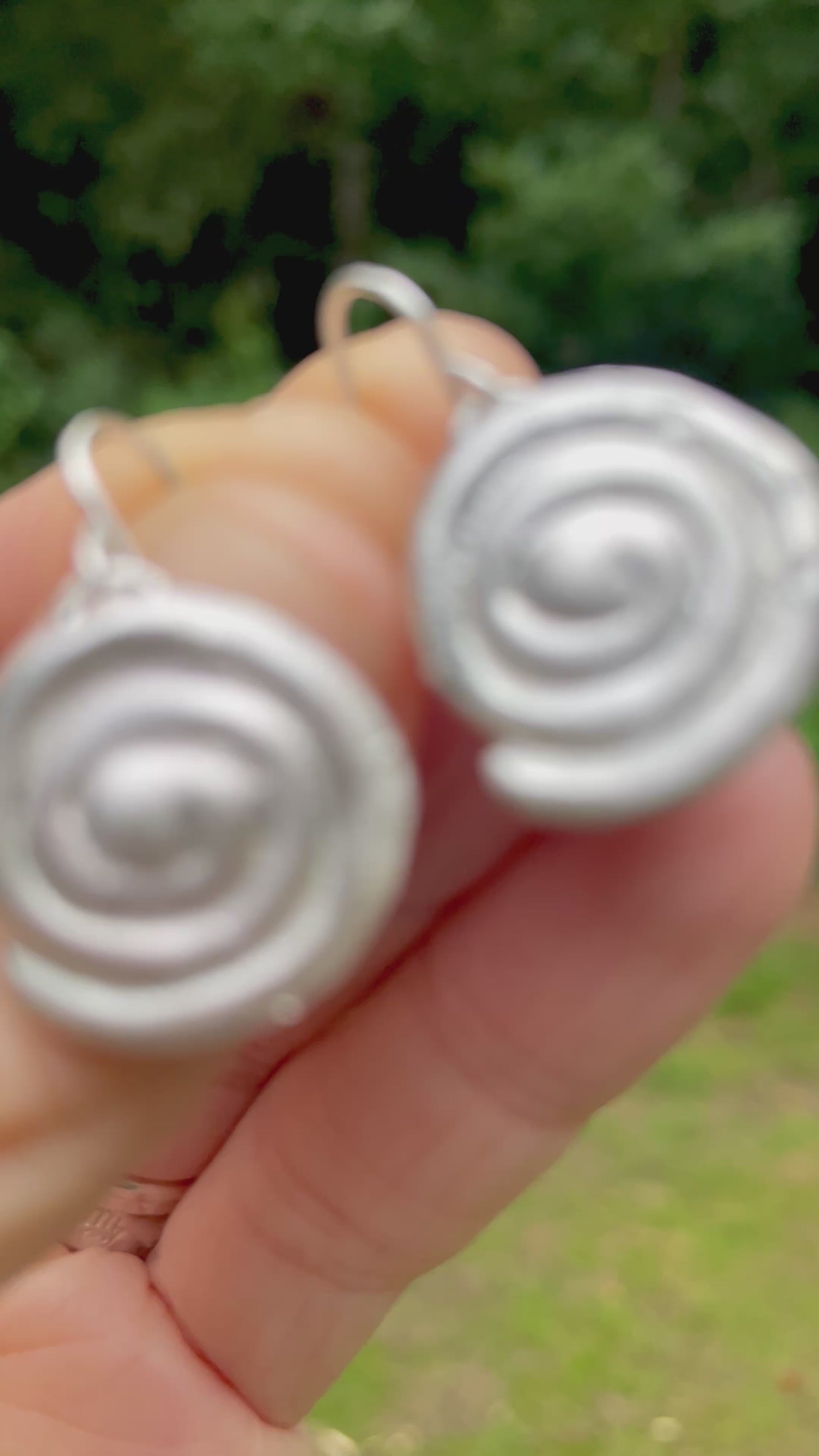 silver sandcast spiral earrings held in hand with green forest background