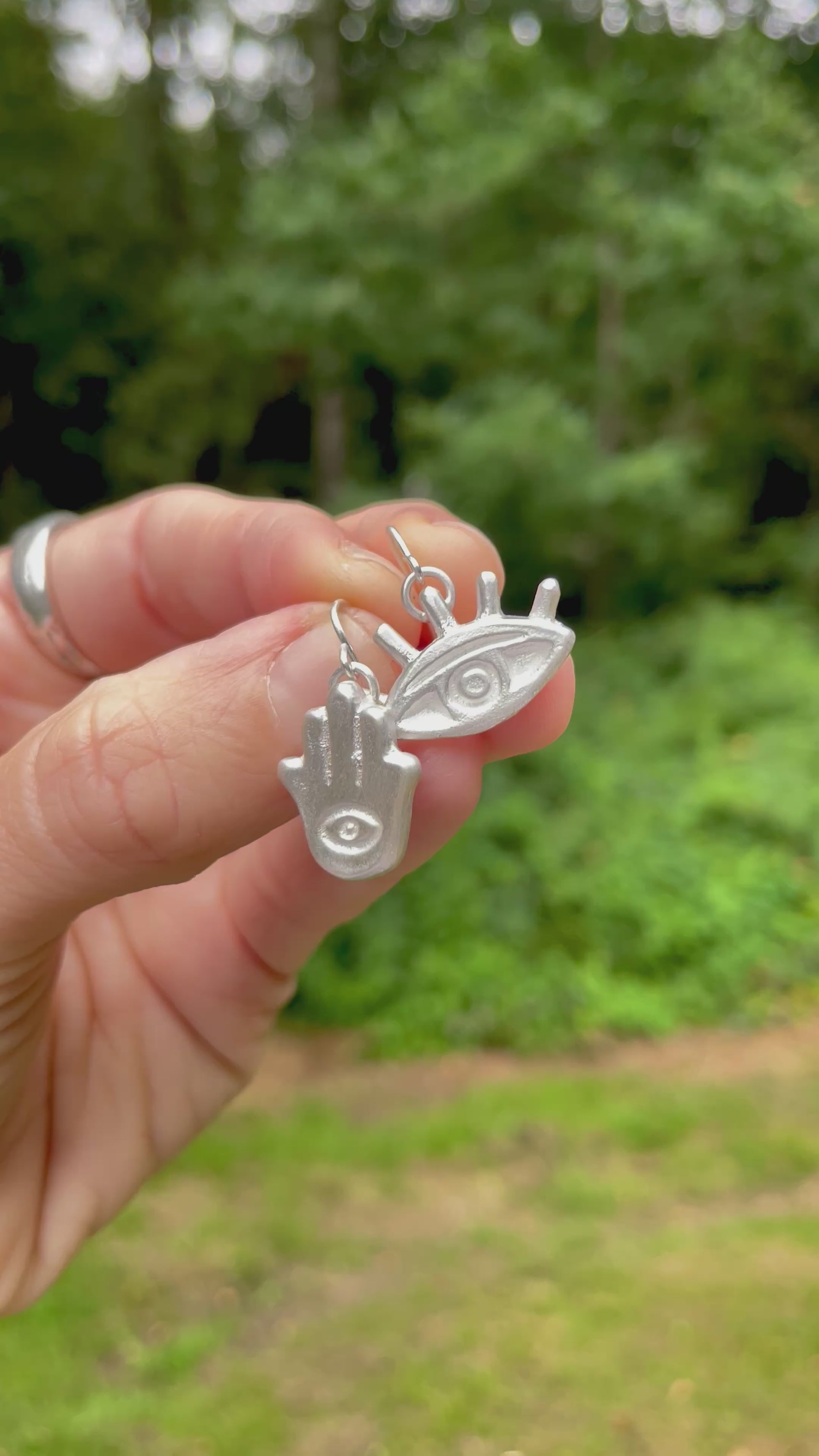 Hamsa hand and eye silver sandcast earrings held in hand with blurred green background