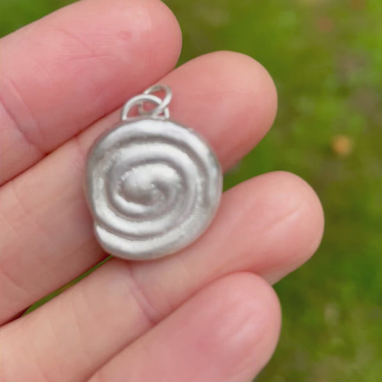 sterling silver sandcast pendant held on fingers with a green grass background