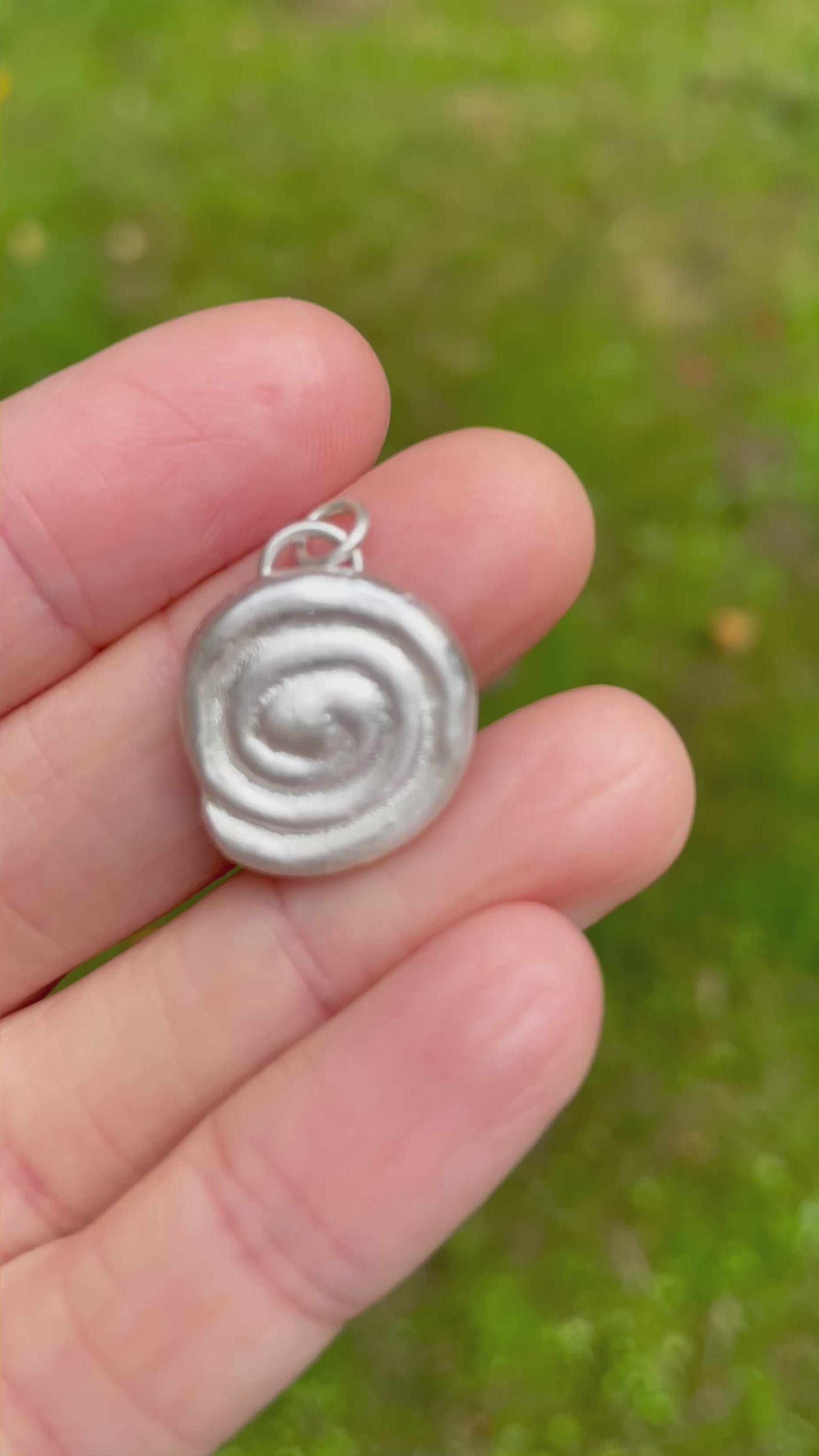 sterling silver sandcast pendant held on fingers with a green grass background