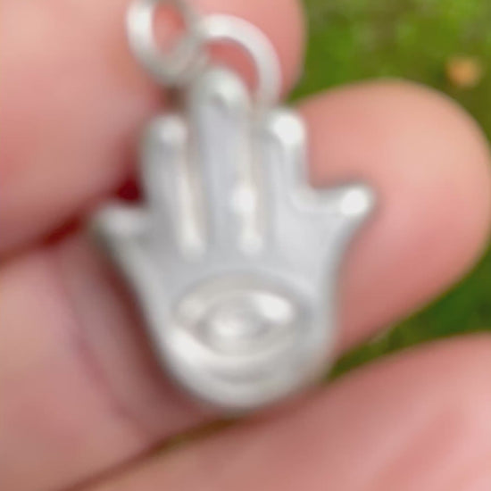 silver sandcast hamsa hand pendent held in hand with green grass background