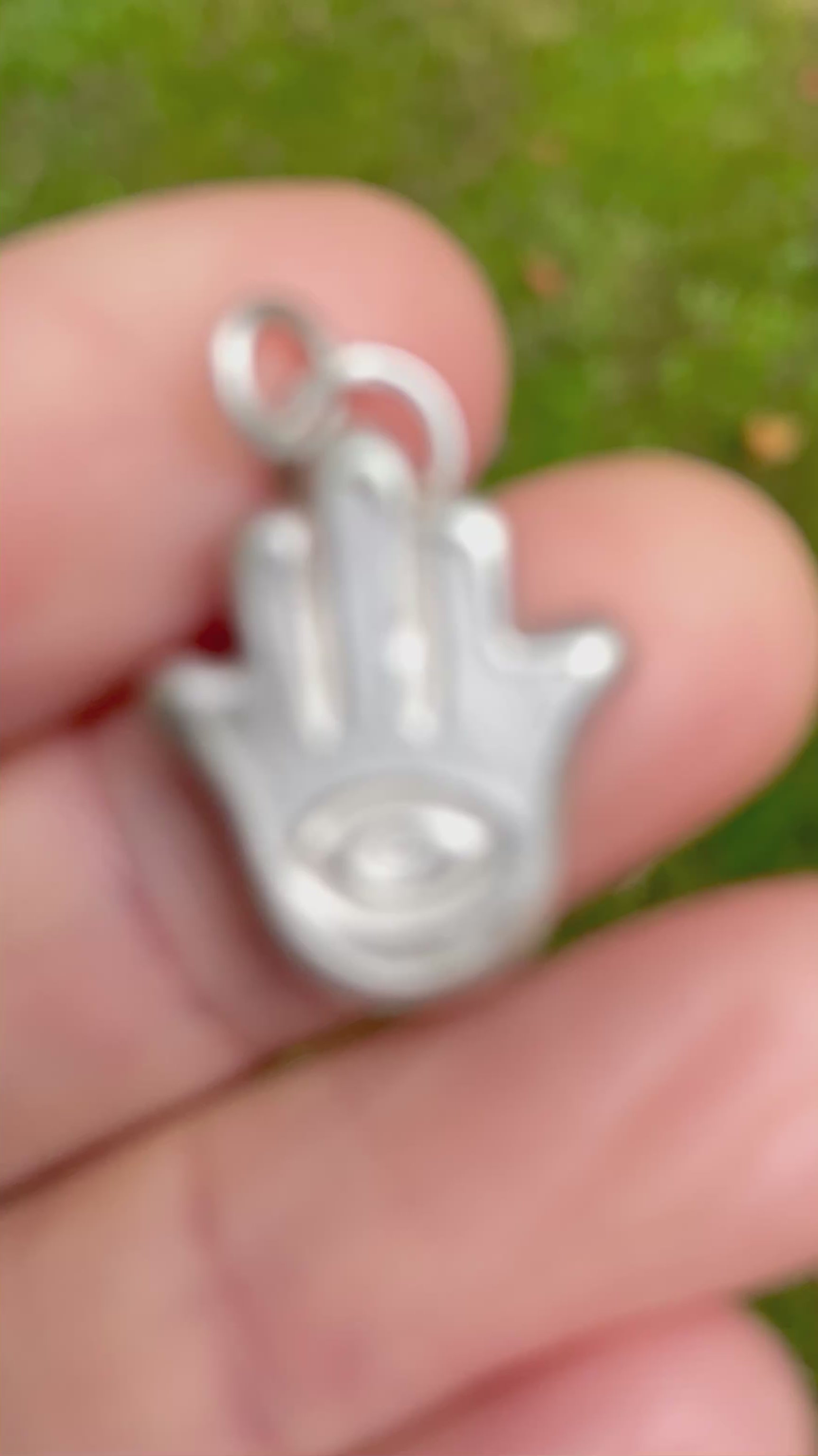 silver sandcast hamsa hand pendent held in hand with green grass background