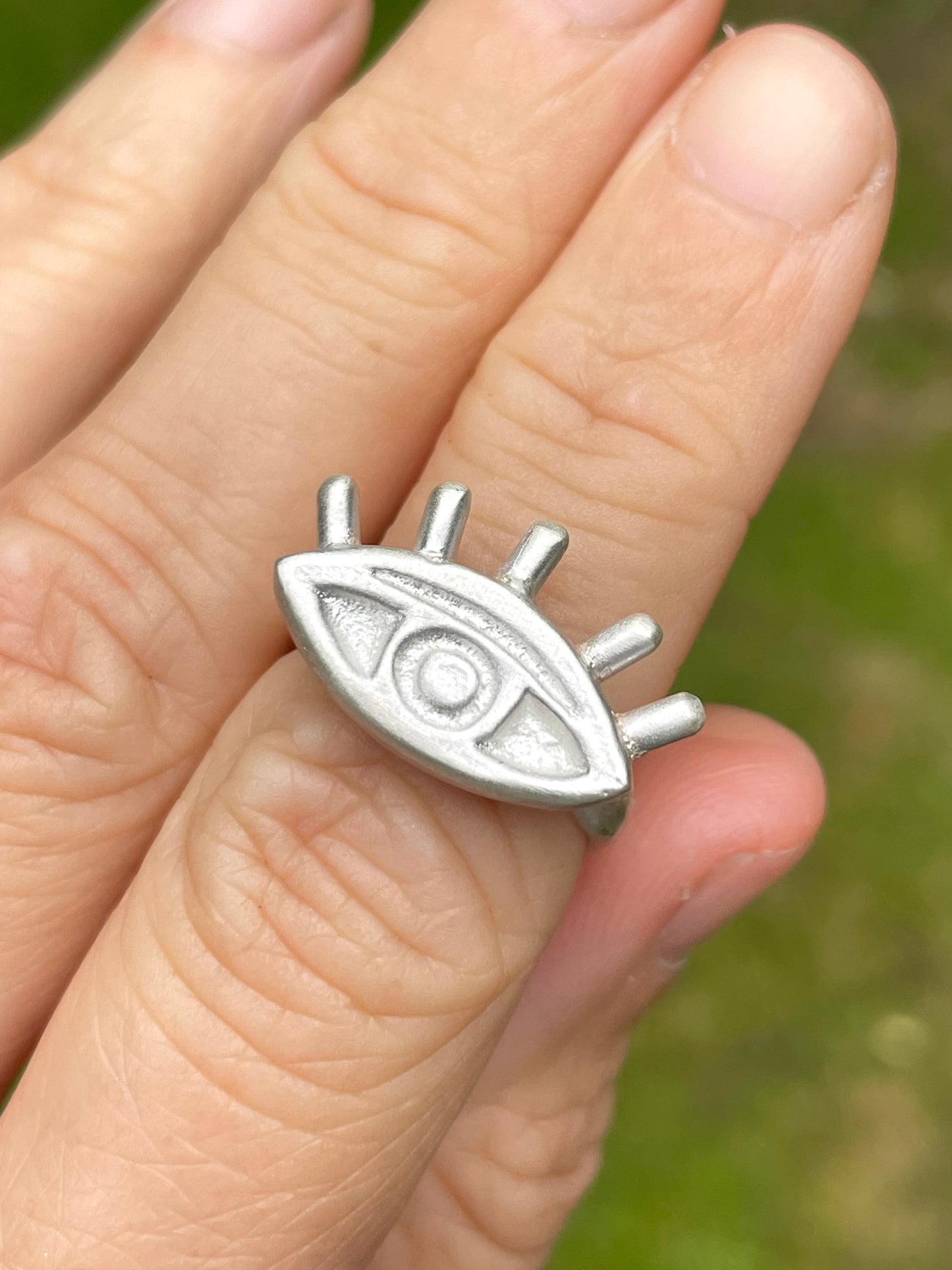 Silver sandcast eye-shaped pendant on a finger with a blurred green background