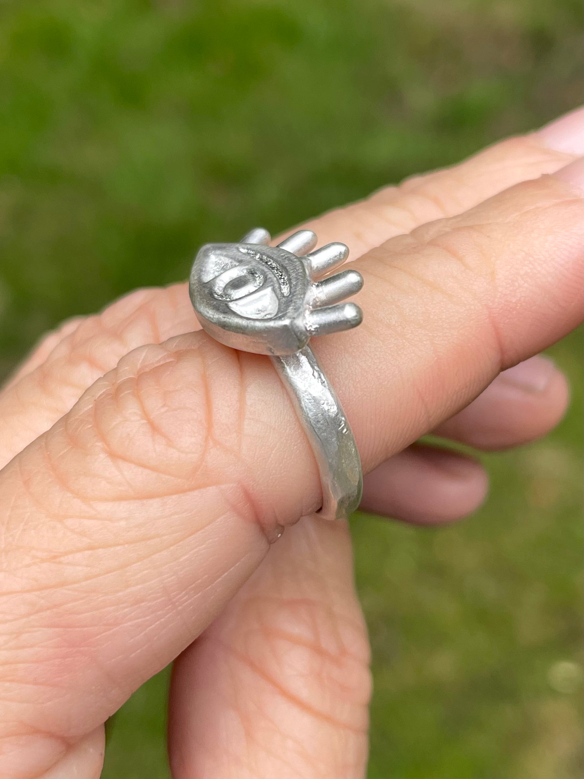 Silver eye shaped ring with a unique design on a finger against a blurred green background