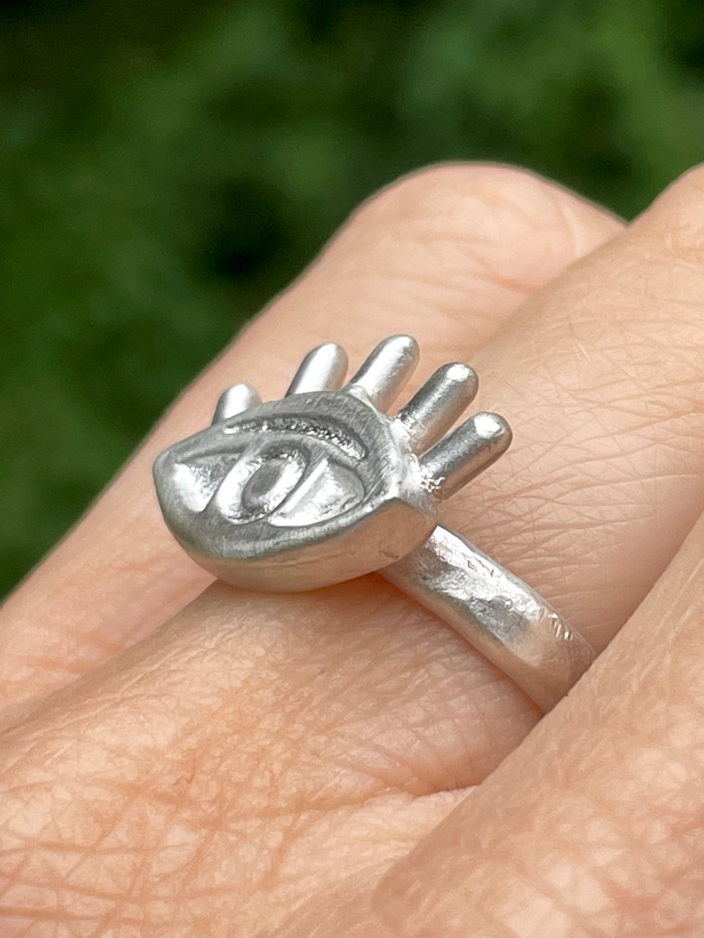 Silver eye-shaped ring on a finger with a blurred green background