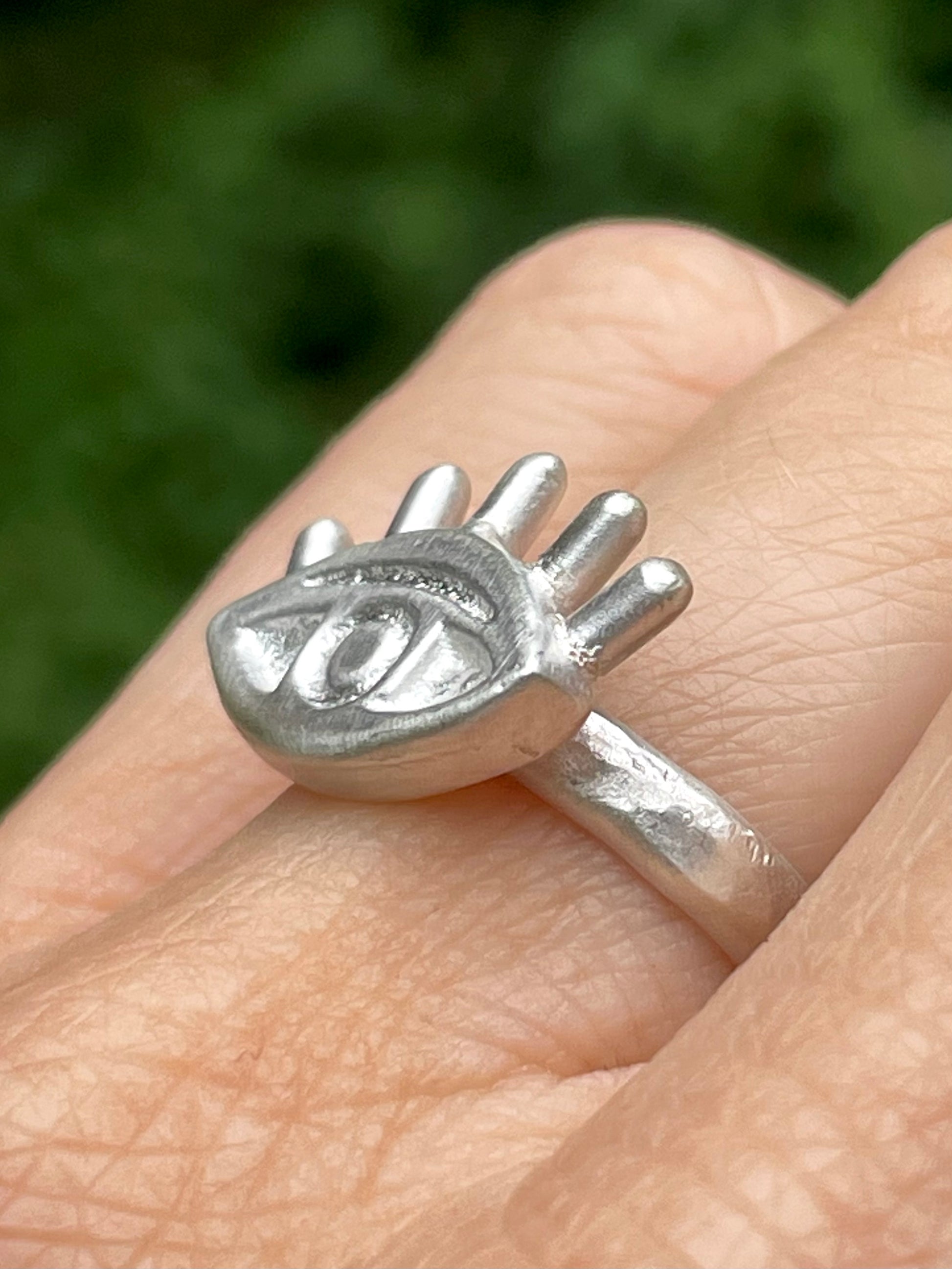 Silver eye-shaped ring on a finger with a blurred green background