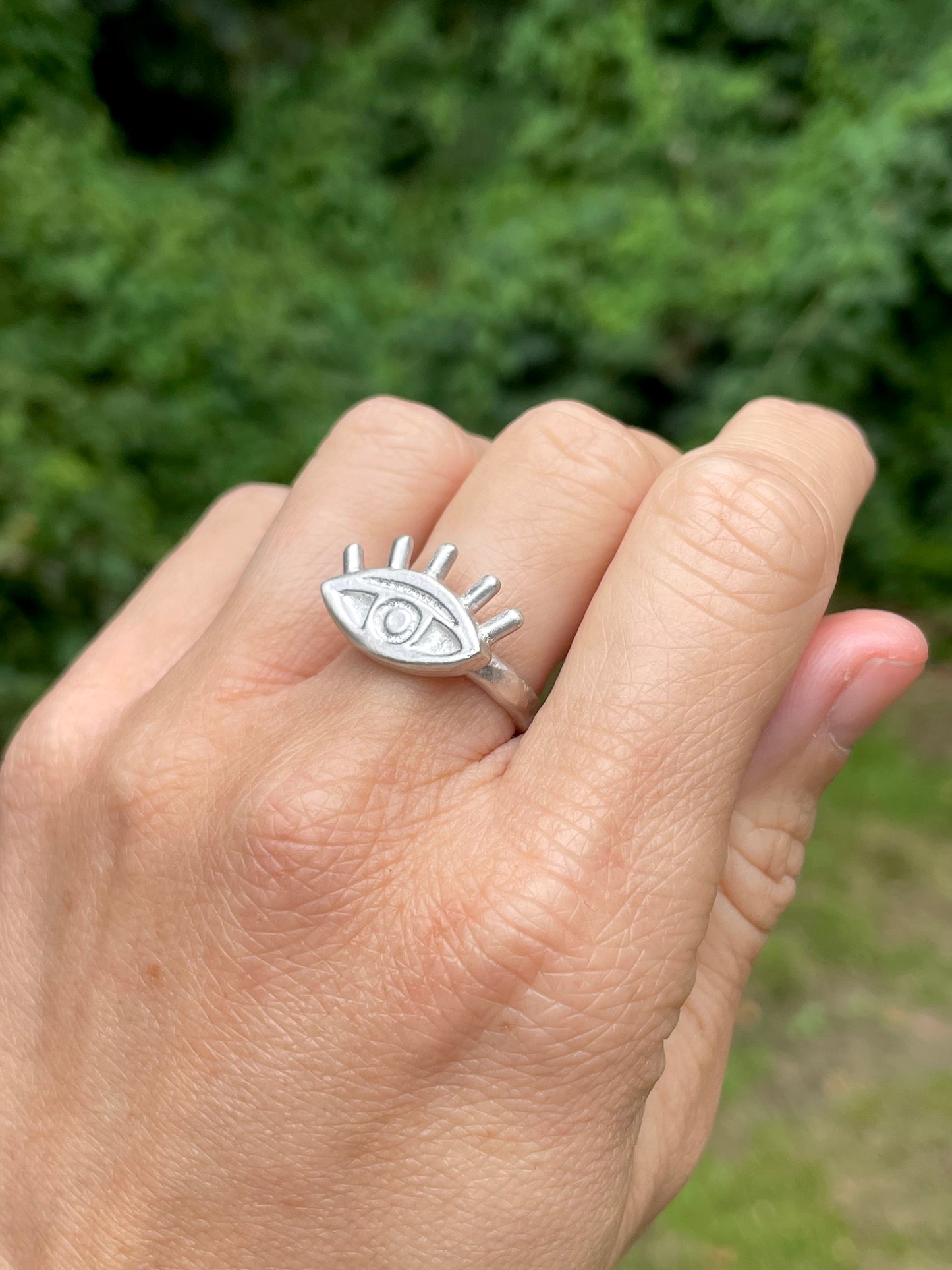 Silver eye-shaped ring on a person's finger with a blurred green background