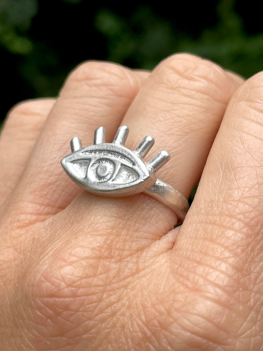 Silver sandcast eye-shaped ring on a finger with a blurred green background
