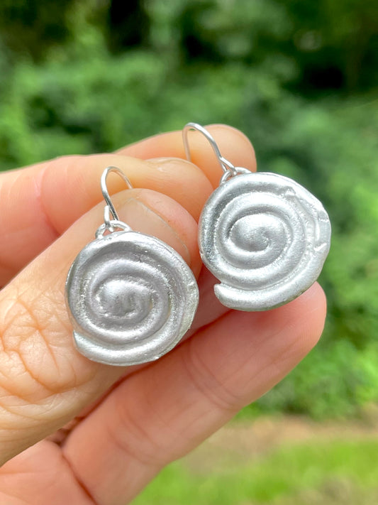 Silver sandcast spiral earrings held in a hand with a blurred green background