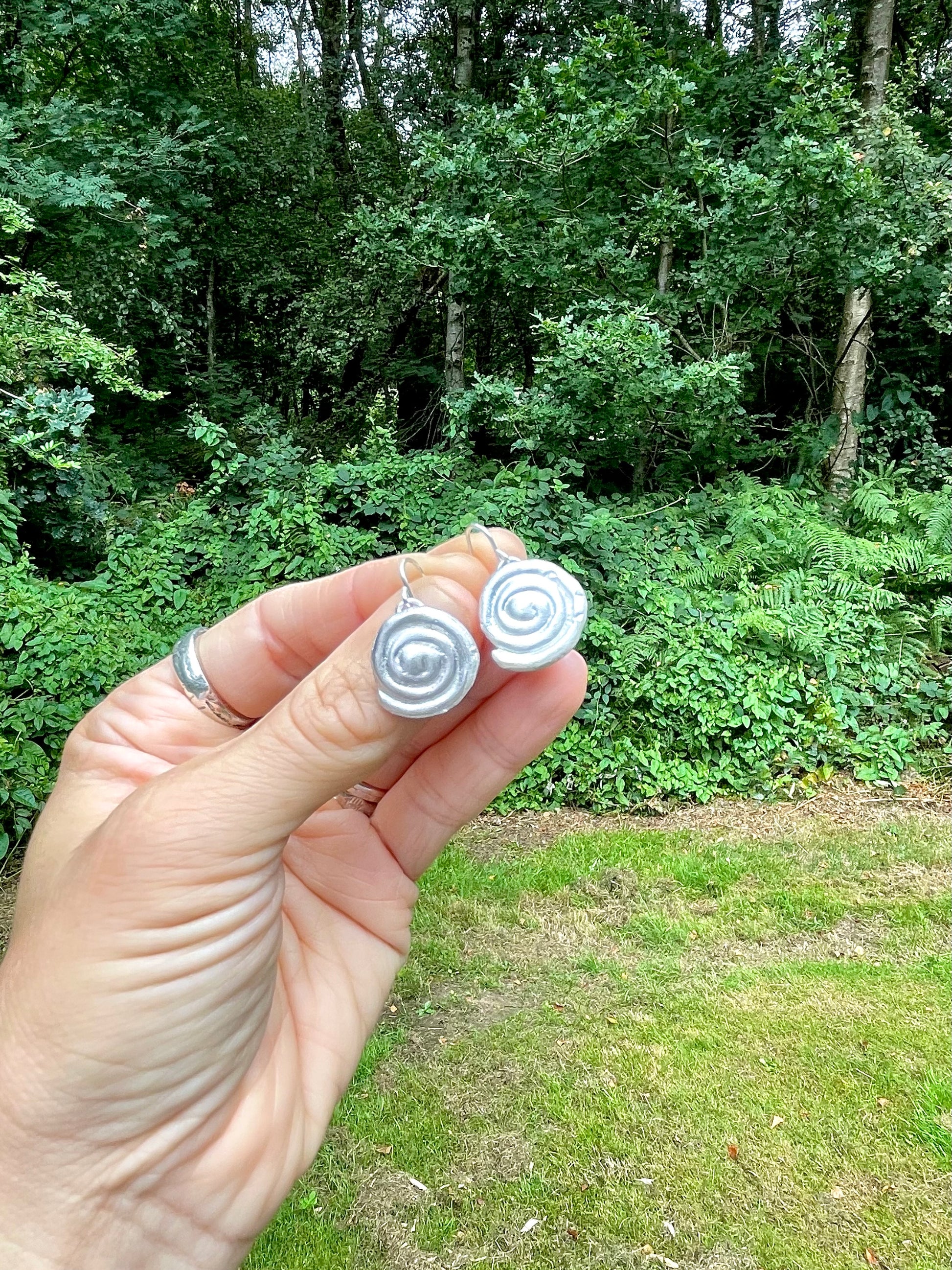 Silver sandcast spiral earrings held in front of a forest background