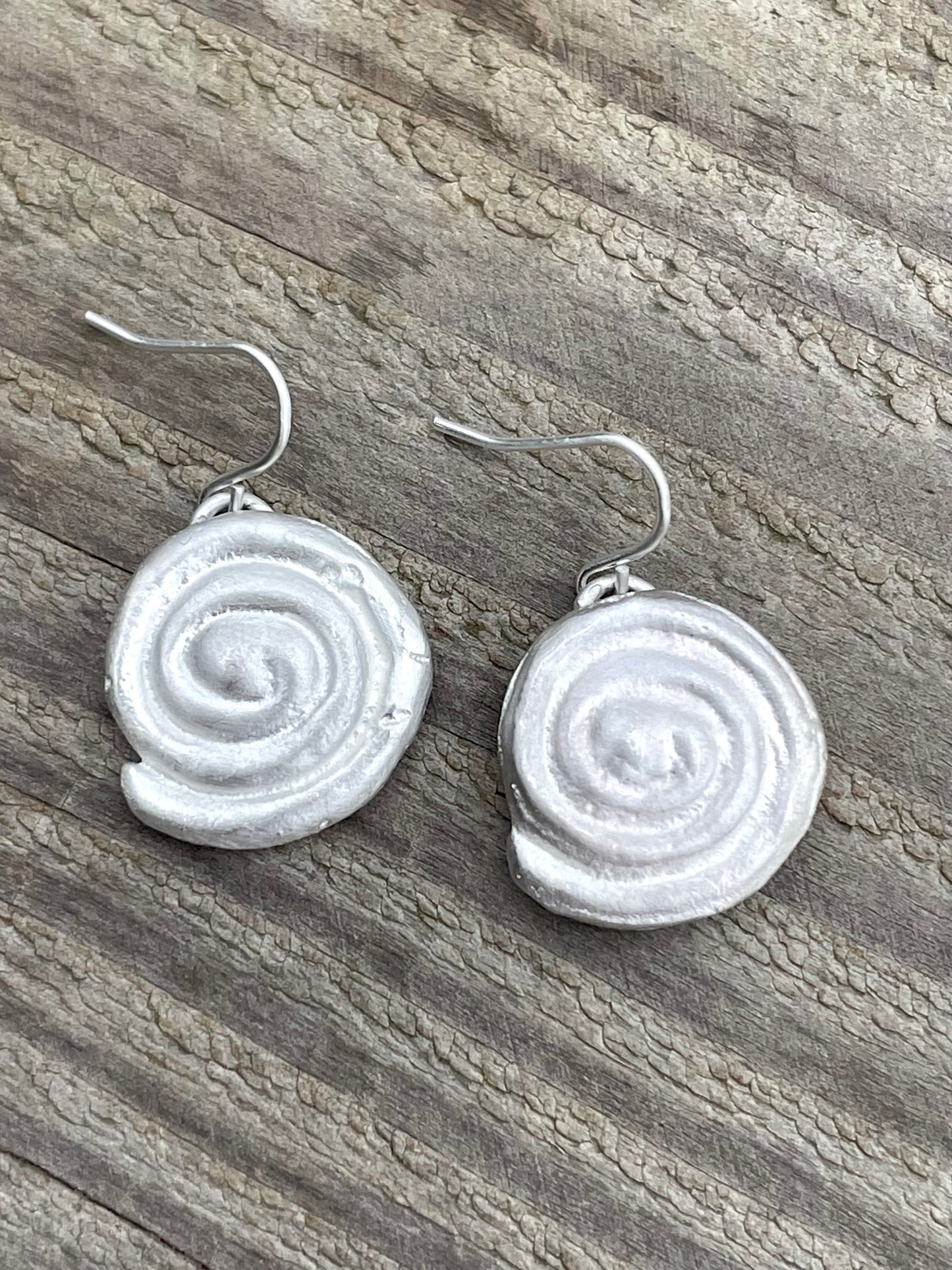 Silver sandcast spiral earrings on a wooden surface