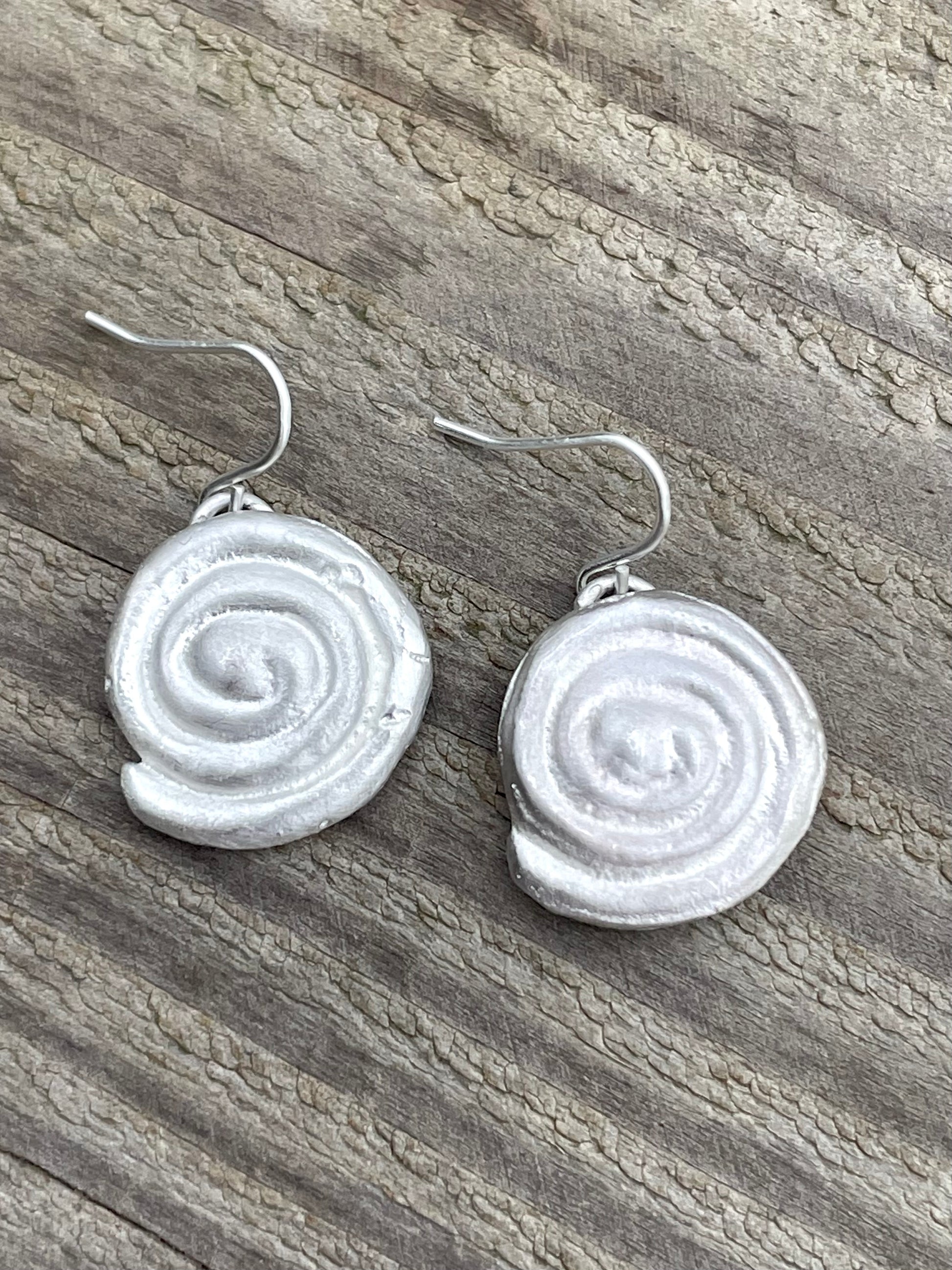 Silver sandcast spiral earrings on a wooden surface