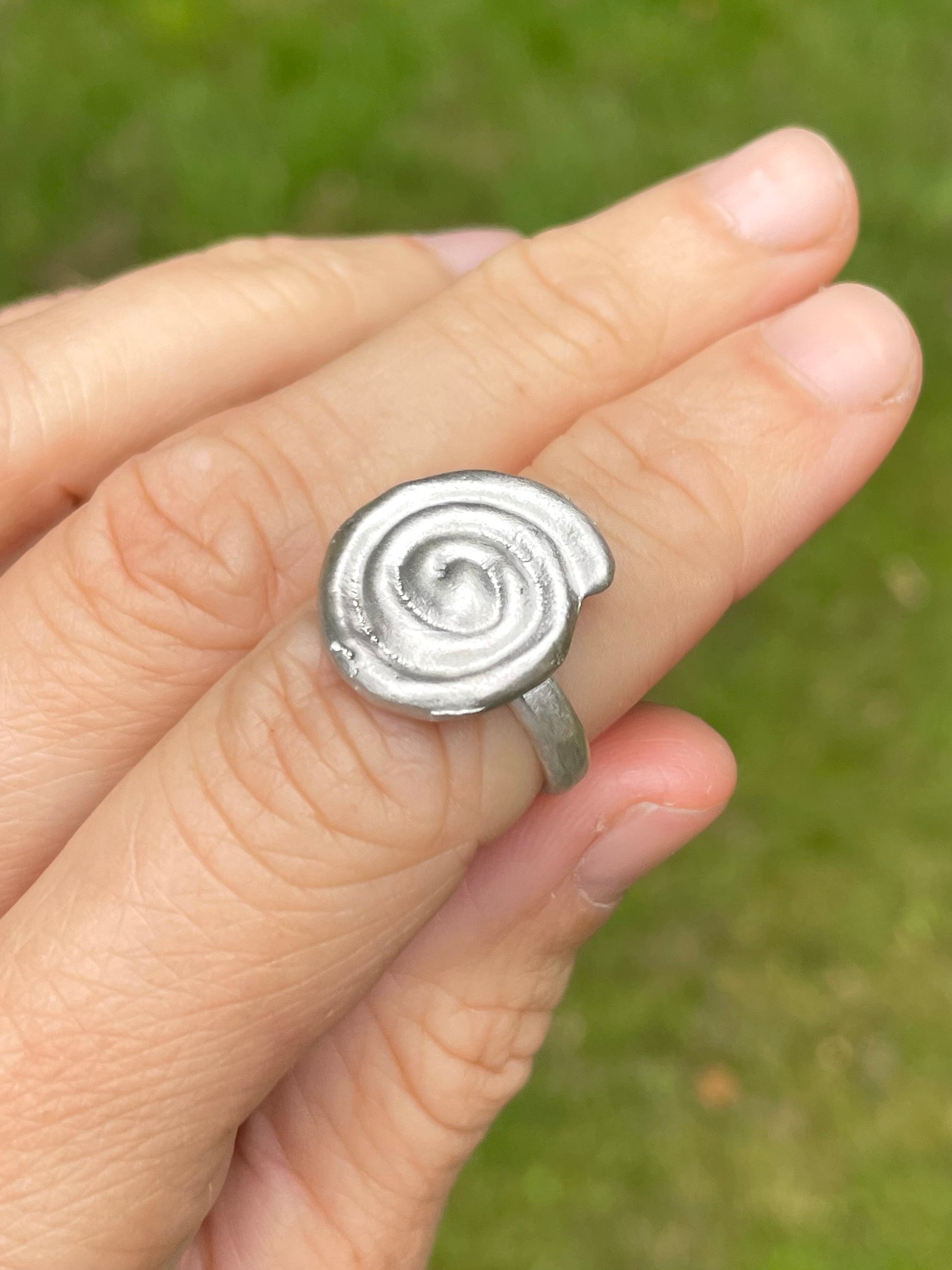 Silver sandcast spiral ring on a finger with a blurred green background