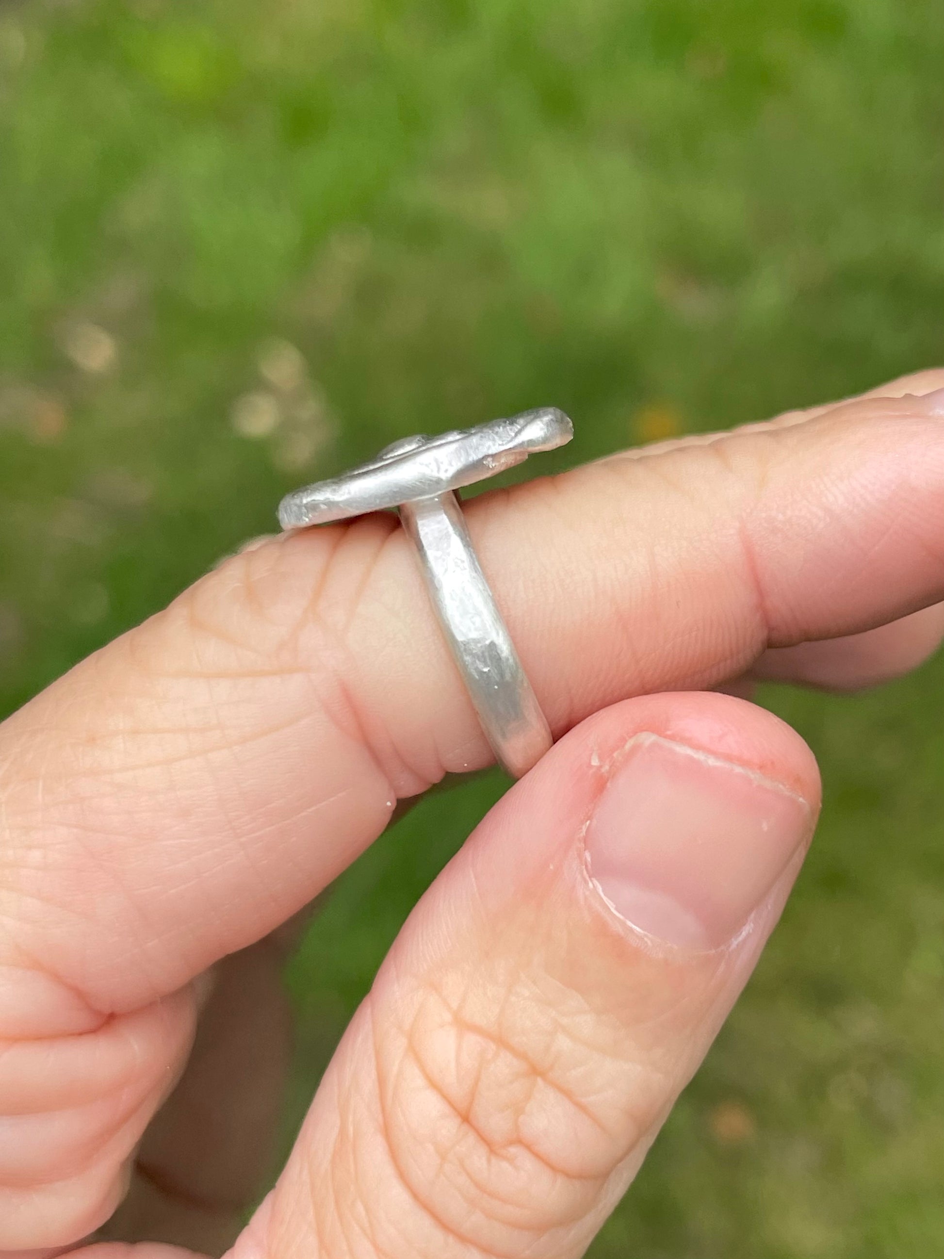 Silver sandcast ring on a finger with a blurred green background