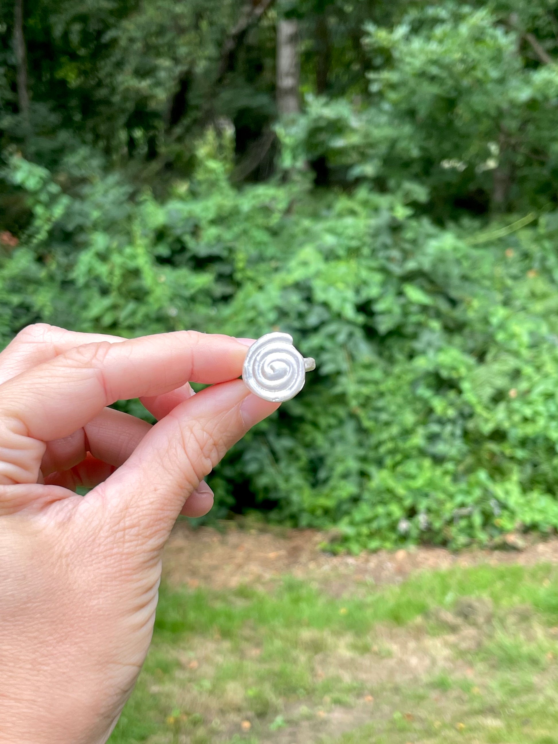 Hand holding a white sandcast silver spiral ring against a blurred green outdoor background