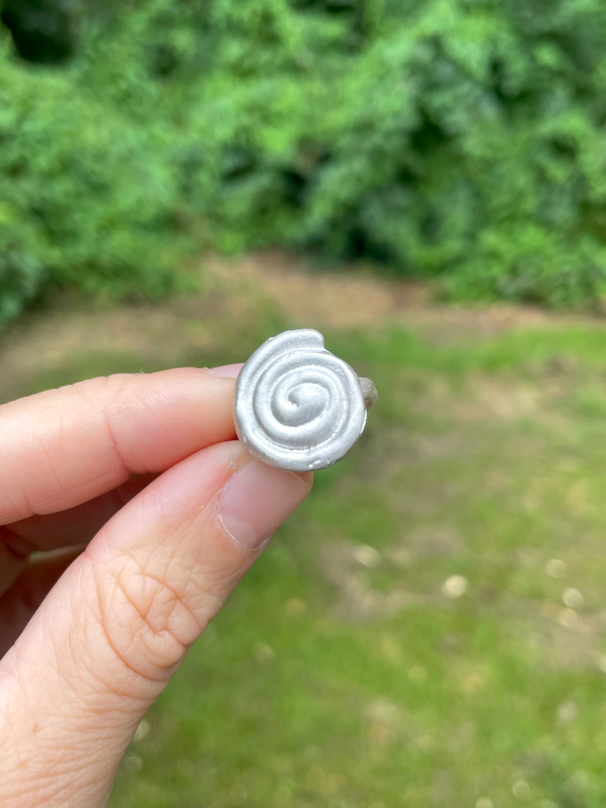 Silver sandcast spiral ring held by a hand with a blurred green outdoor background