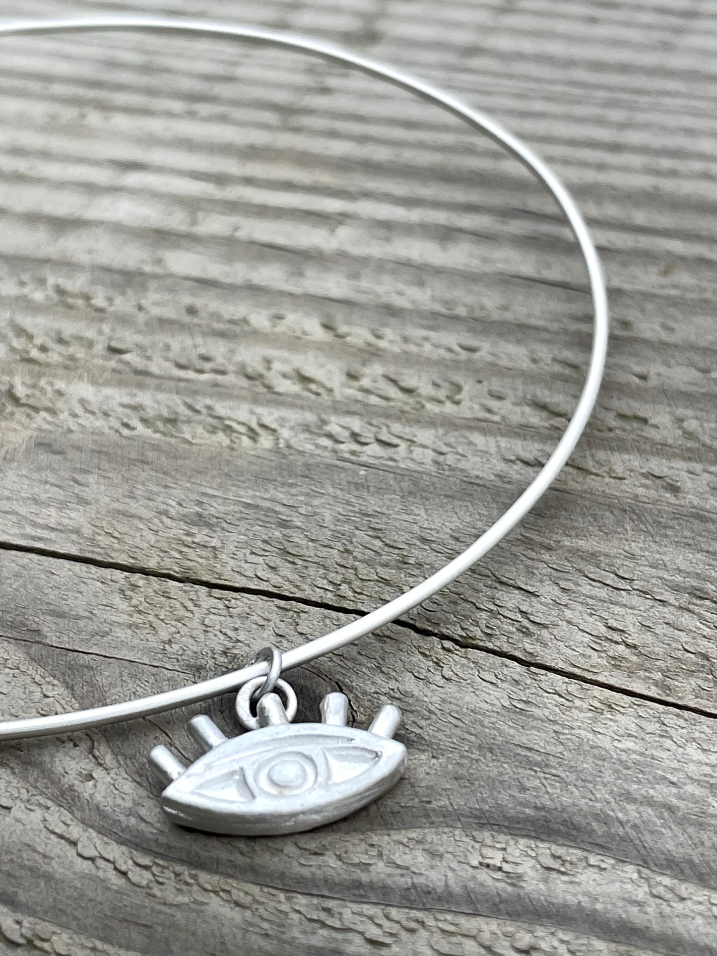 Silver choker necklace with an eye pendant on a wooden surface