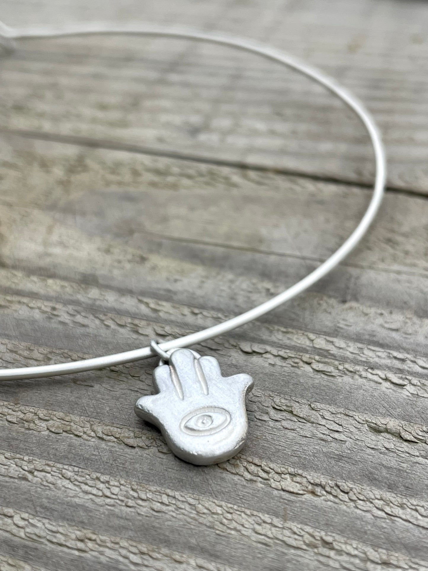 Silver choker necklace with a sandcast Hamsa hand pendant on a wooden surface