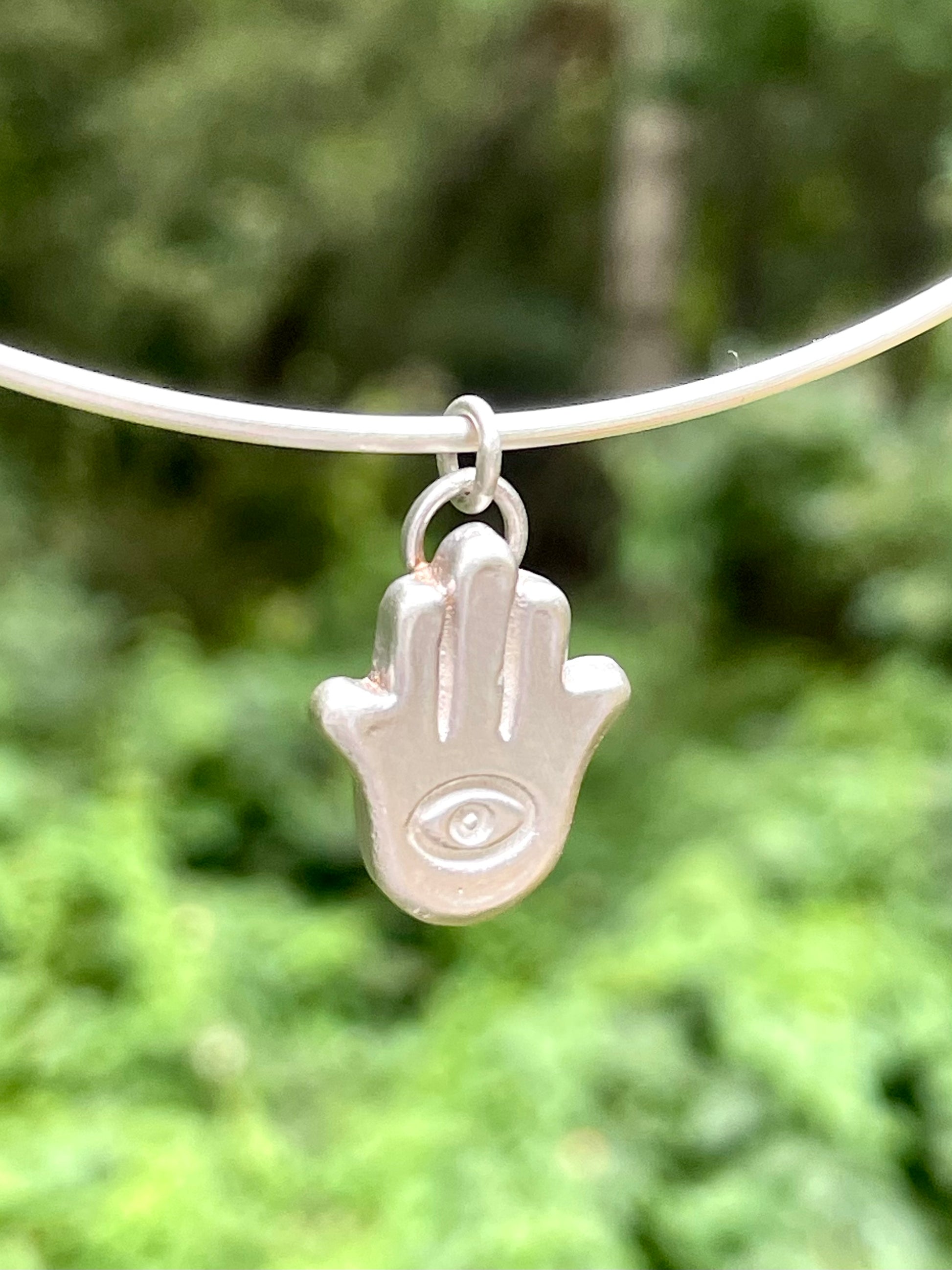Silver Hamsa hand charm on a thin silver chain against a blurred green background