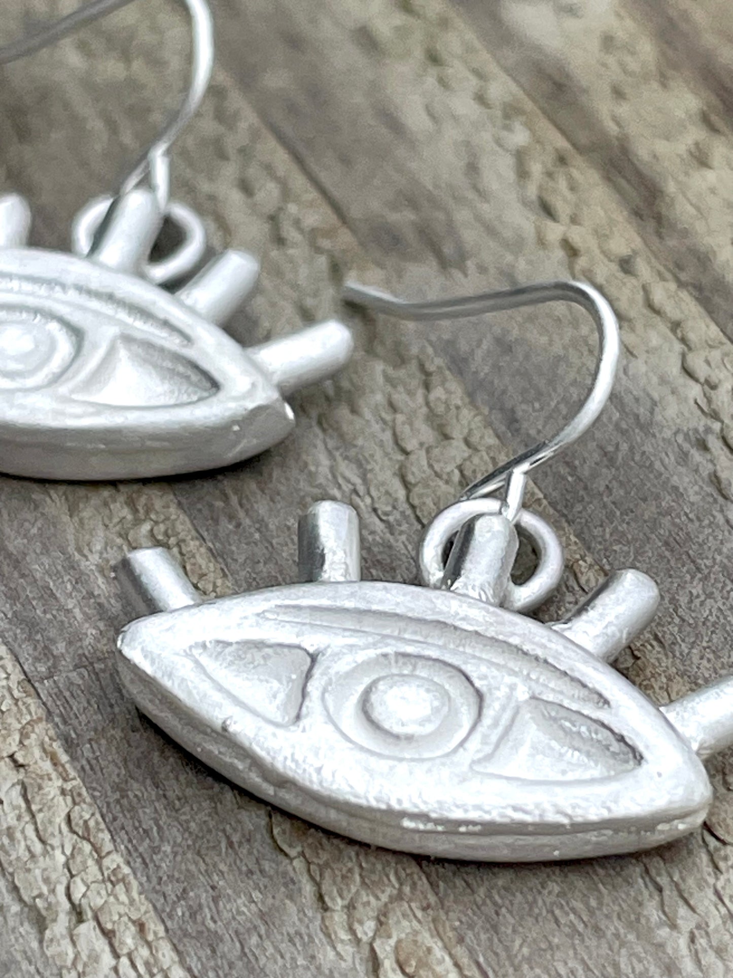 Silver sandcast eye-shaped earrings on a wooden surface