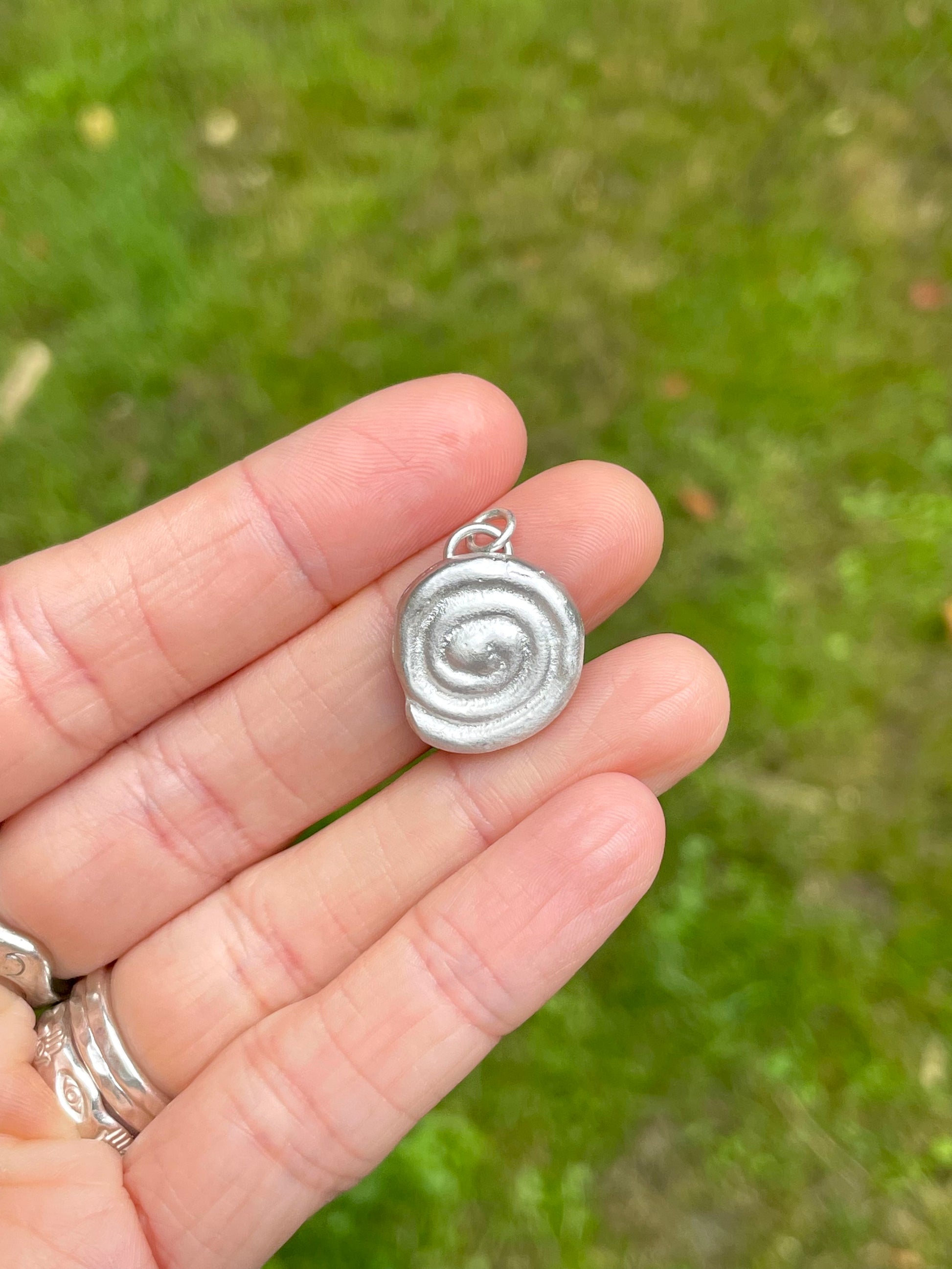 Silver spiral pendant held in a hand with a blurred green background