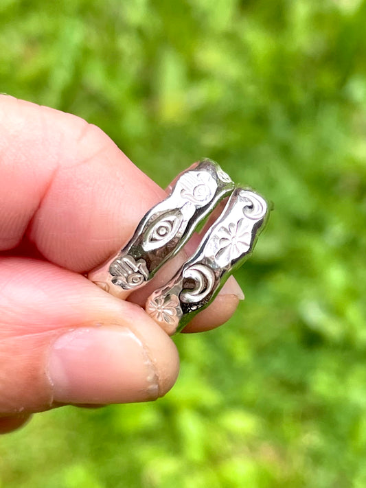 Silver stamped band rings with intricate designs held between fingers against a blurred green background