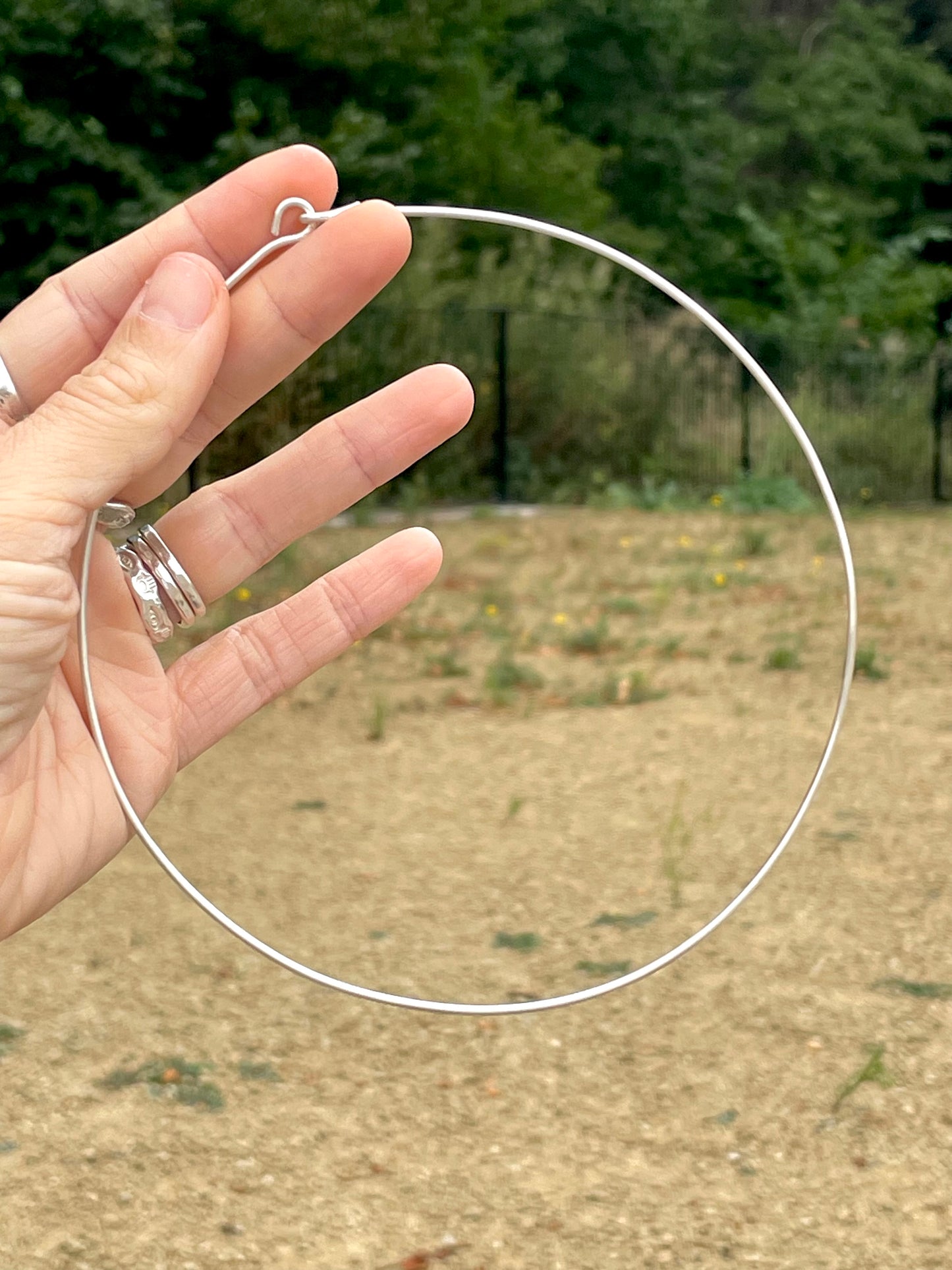 Hand holding a silver silver wire choker necklace with a blurred outdoor background